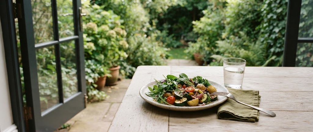 A simple lunch of salad and roasted vegetables on a wooden table beside an open garden door