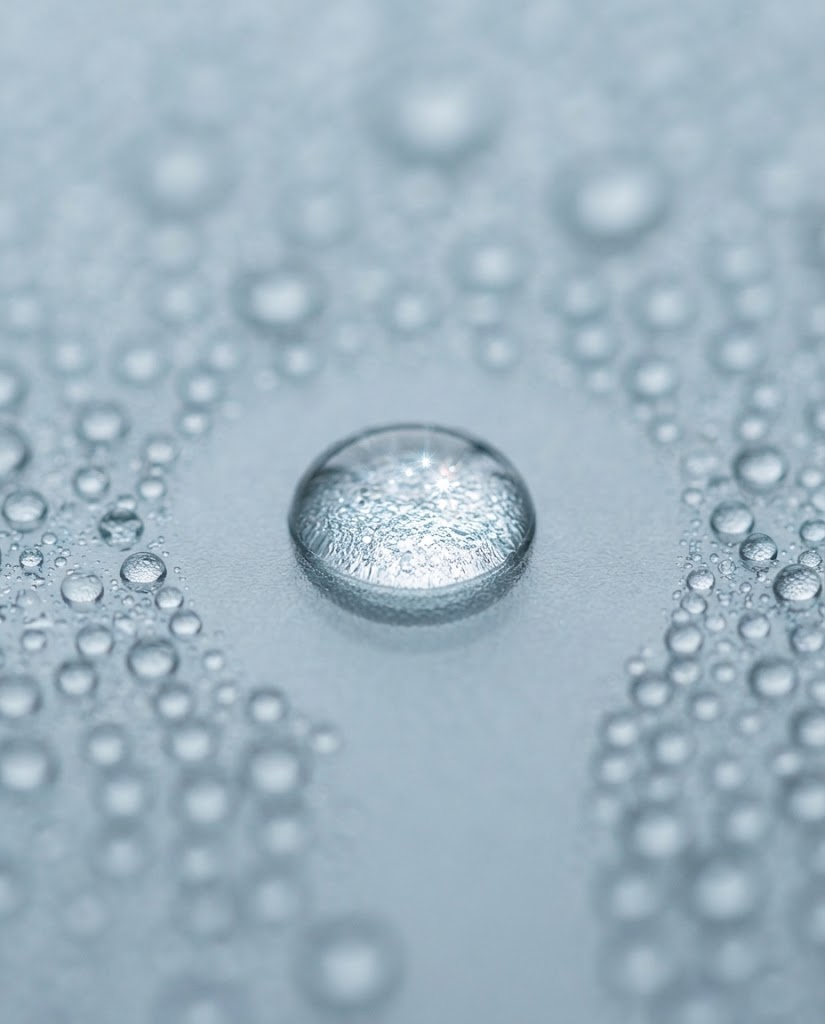 Extreme macro of clear water droplets beading on smooth pale grey glass in cool daylight