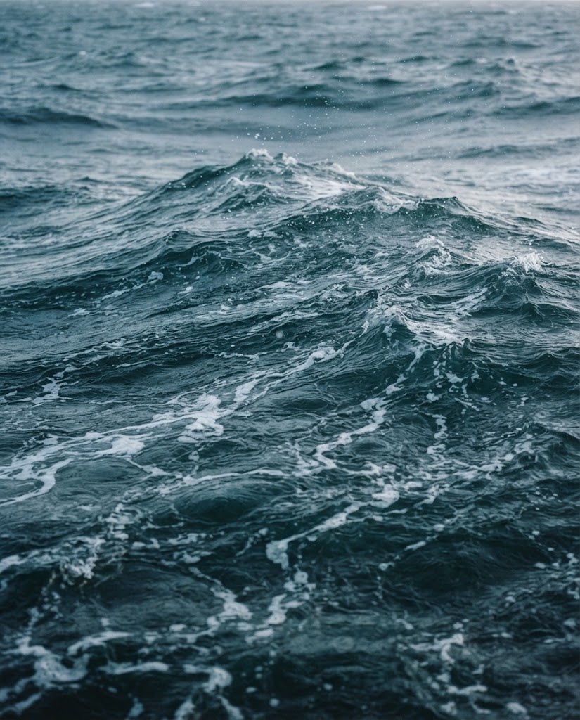 The surface of a cold north Atlantic sea, deep blue-green water with white foam threading across it in low afternoon light